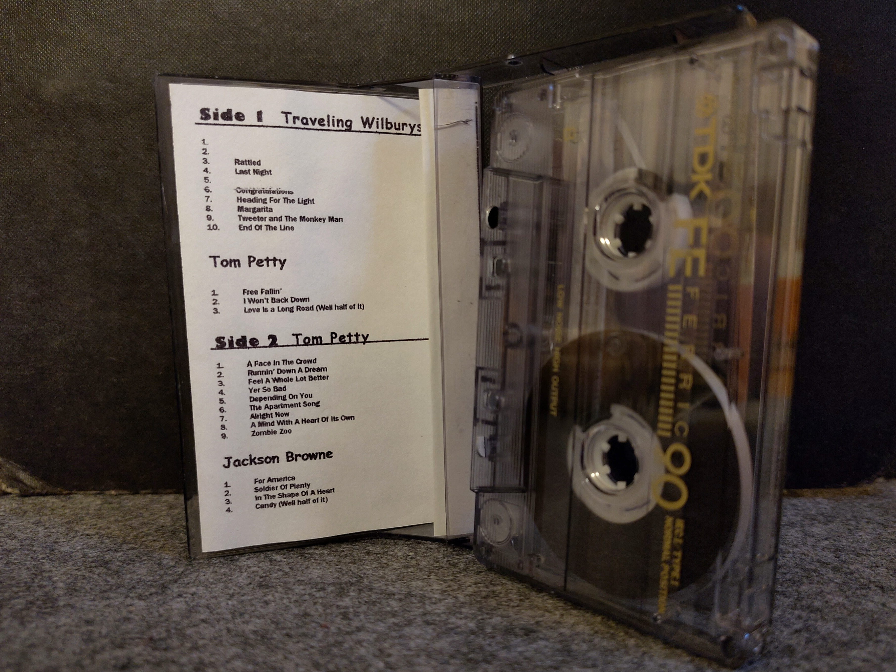 Open cassette tape case with insert. Photo of an audio cassette, standing next to its open case. Inside there is a home printed paper insert listing the songs on the cassette.